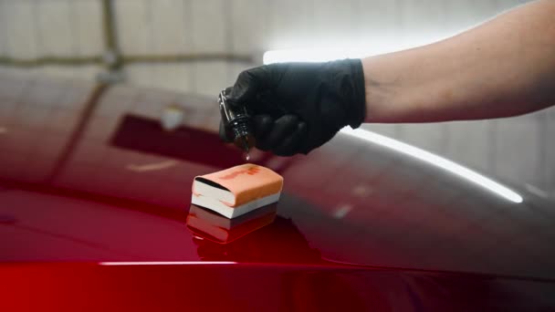 Close-up van een met de hand druppelende vloeibare coating op een sponsapplicator op een motorkap. Voorbereiding voor het aanbrengen van een speciale coating op een autooppervlak. - Video