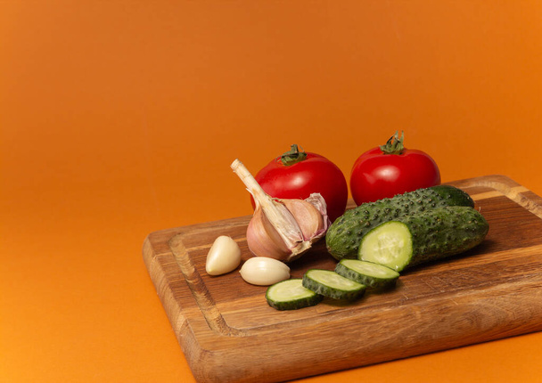 Sliced cucumber, tomatoes and garlic on wooden cutting board. Tomatoes with green ponytails. Healthy food. Copy space. High quality close up photo - Фото, зображення