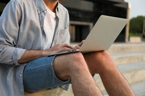 Young man sits in steps and working in laptop outdoor. Freelancer - Zdjęcie, obraz