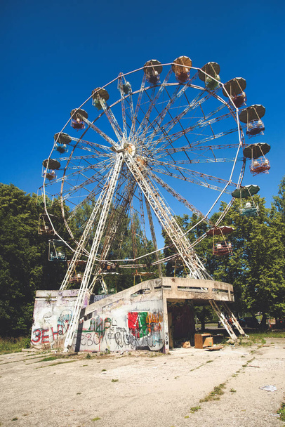 Een oud roestig reuzenrad in een gesloten verlaten USSR pretpark. Droevige post apocalyps sfeer in zonnige zomerdag. - Foto, afbeelding