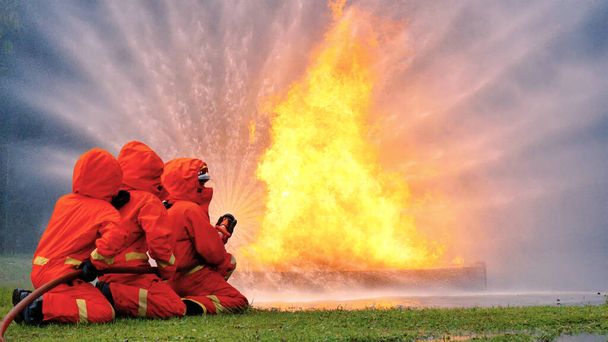 Пожарный борется с пламенем с помощью пожарного шланга химического распылителя воды. Пожарный носит каску, костюм для защиты. Спасательные учения на огнетушителе - Фото, изображение