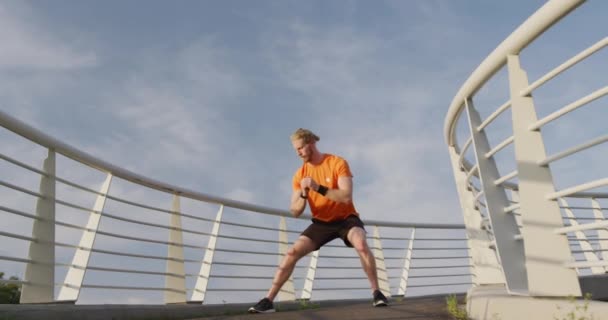 A young athletic Caucasian man exercising on a footbridge in a city, stretching out in slow motion. Healthy urban active lifestyle. - Filmagem, Vídeo