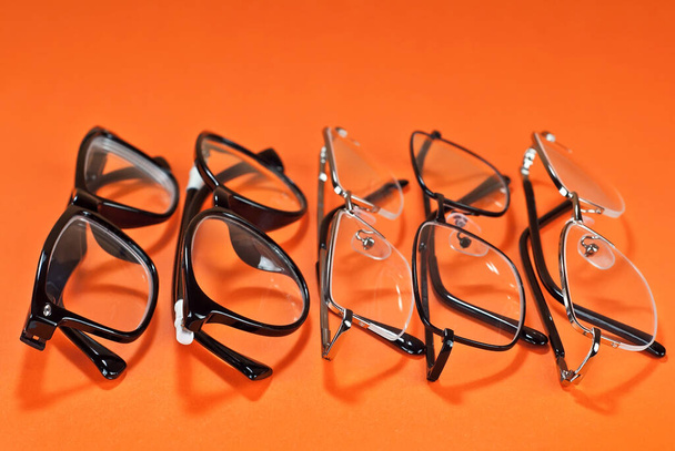 Different types of glasses on an orange background close up. Glasses with rectangular and round frames. - Photo, image