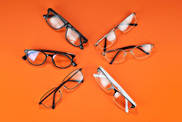 Different types of glasses on an orange background close up. Glasses with rectangular and round frames.  - Fotografie, Obrázek