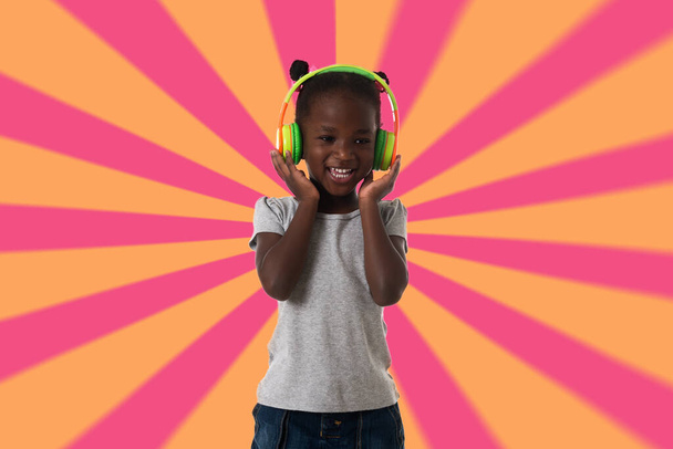 Music, childhood and technology concept.Lovely happy little girl with headphones over geometric background - Photo, Image