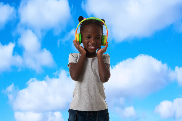 Musique, enfance et concept de technologie.Belle petite fille heureuse avec écouteurs sur fond de ciel bleu - Photo, image