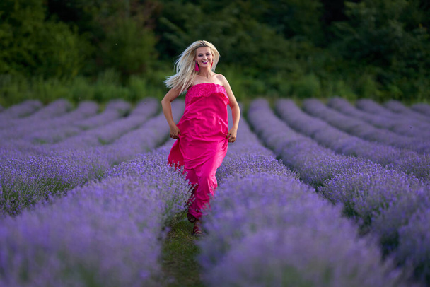 Young blonde woman in pink dress in a lavender field with various poses - Фото, зображення