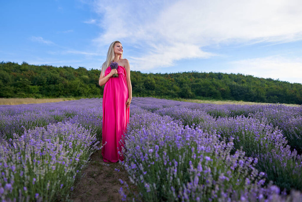 Young blonde woman in pink dress in a lavender field with various poses - 写真・画像