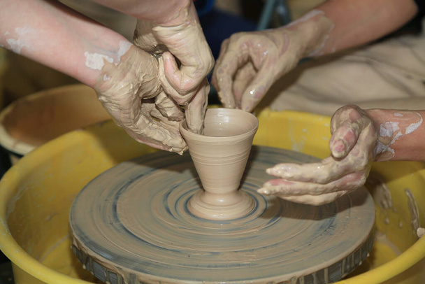 Erstellen eines Tonproduktes auf einer Töpferscheibe in einer Töpferei. Hände gleiten auf Lehm. Kunst - Foto, Bild