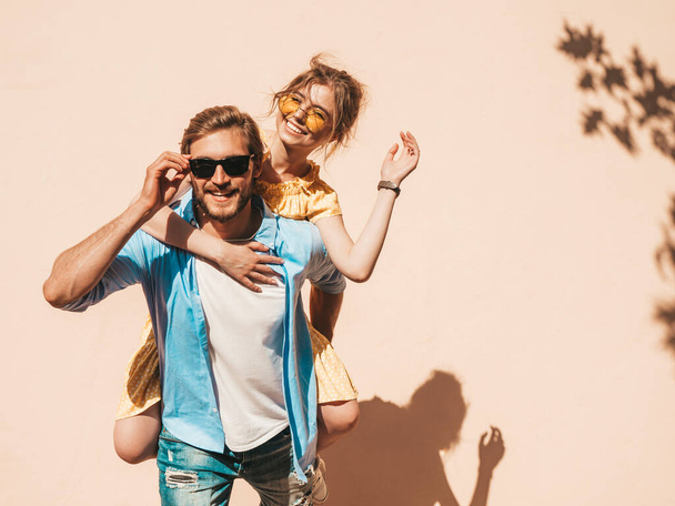Portrait of smiling beautiful girl and her handsome boyfriend. Woman in casual summer dress and man in jeans. Happy cheerful family. Female having fun in the street near wall - Foto, Imagen