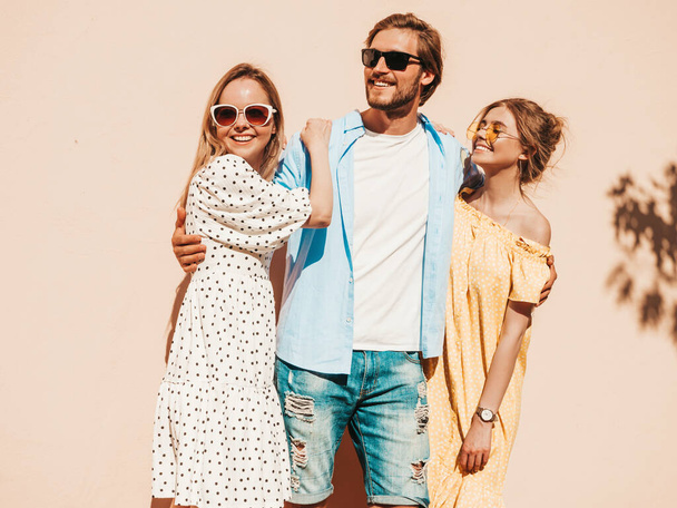 Group of young three stylish friends posing in the street. Fashion man and two cute girls dressed in casual summer clothes. Smiling models having fun in sunglasses.Cheerful women and guy going crazy - Photo, image