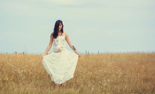 Romantic portrait in vintage tones and texture woman in a lacy clothes standing in the  field and enjoying herself and nature. The concept of self love and harmony with the environment - Foto, afbeelding