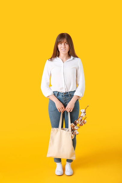 綿の花と色の背景にショッピングバッグを持つ美しい若い女性 - 写真・画像