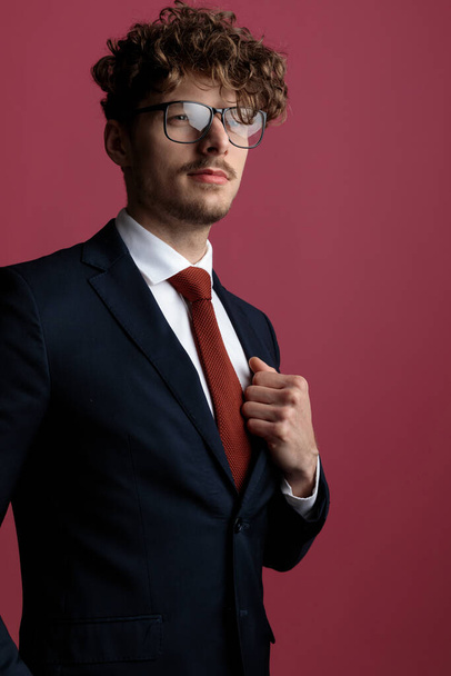 sexy zakenman met stijl vaststelling van zijn jas, het dragen van bril en weg te kijken op roze studio achtergrond - Foto, afbeelding