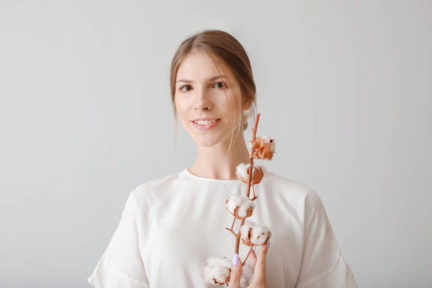 Beautiful young woman with cotton flowers on light background - Foto, afbeelding