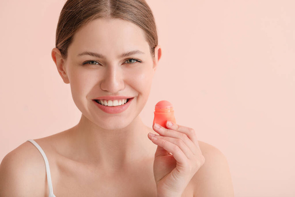 Beautiful young woman with lip balm on color background - Foto, afbeelding