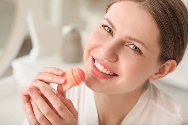 Beautiful young woman with lip balm at home - Foto, afbeelding