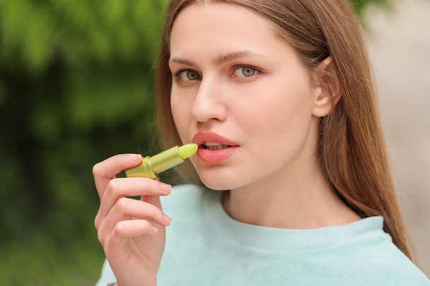 Schöne junge Frau mit Lippenbalsam im Freien - Foto, Bild