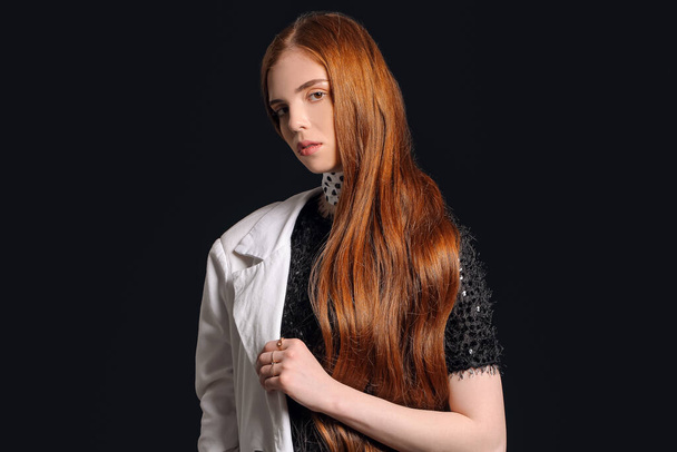 Beautiful young redhead woman on dark background - 写真・画像