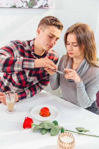 Nuori poika ja tyttö yrittävät ottaa ruokakuvan älypuhelimella, kun taas aamiainen kahvilassa. - Valokuva, kuva