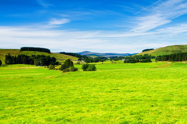 Campos verdes rodantes bajo un cielo azul tranquilo. Colorido panorama sobre los prados de las tierras de labranza de ovejas del valle escocés en Escocia, Reino Unido
 - Foto, imagen