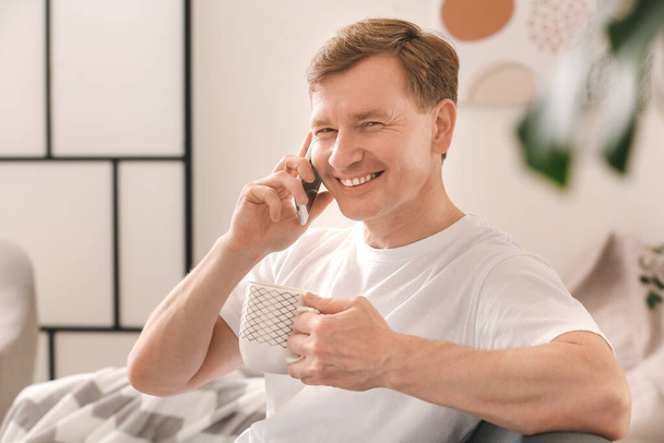 Evde telefonla konuşurken çay içen yakışıklı adam. - Fotoğraf, Görsel
