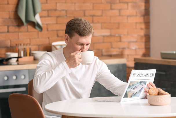 Jóképű férfi újságpapírral teázik otthon. - Fotó, kép
