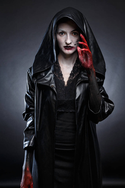Foto de mujer aterradora en capucha de cuero negro con manos rojas
 - Foto, Imagen
