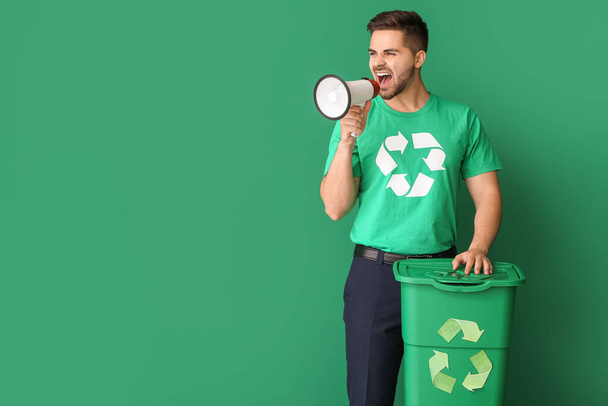 Mężczyzna w koszulce ze znakiem recyklingu, koszem na śmieci i megafonem na tle koloru. Koncepcja ekologiczna - Zdjęcie, obraz
