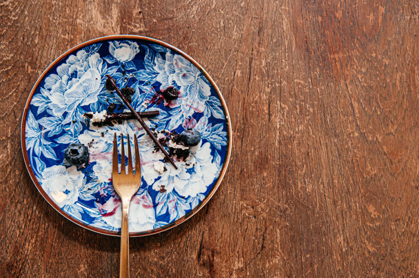 Blueberry-Käsekuchen bereits gegessen hinterließ einen Fleck auf schönen Luxus-Keramikschale mit Messinggabel auf Holztisch - Foto, Bild