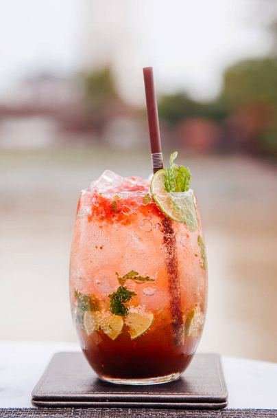 Свежий холодный сладкий и кислый красный коктейль Мохито в красивом стакане с ломтиками лайма и листьями мяты
 - Фото, изображение