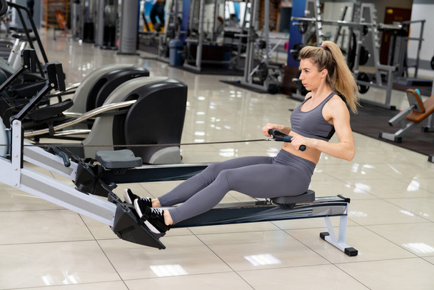 Young woman working out on row machine at gym exercising - Zdjęcie, obraz