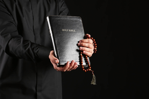 Young priest with Bible on dark background - Photo, Image