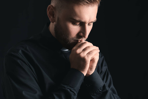 Young priest praying to God on dark background - Photo, image
