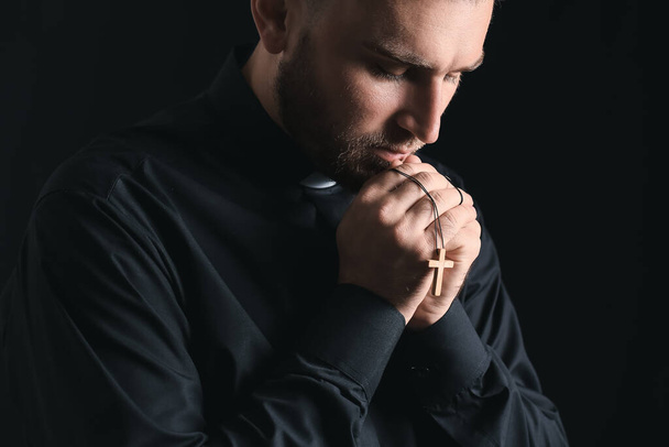 Young priest praying to God on dark background - Photo, Image