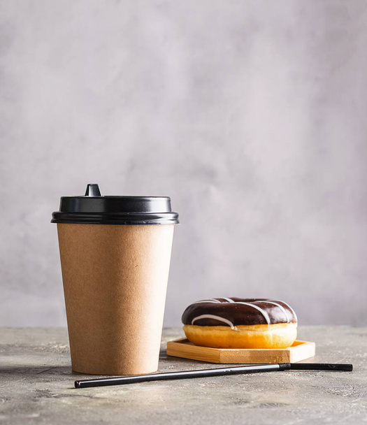 Paper cup with coffee drink or tea donut in chocolate icing on a gray background. Zero West food and drink concept. Vertical frame copy space - Photo, Image