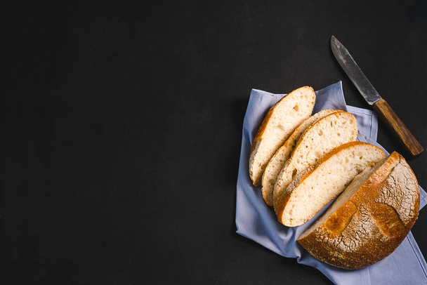 Een broodje vers gebakken brood op een zwarte achtergrond. Het concept van minimalisme voedsel. Vlakke indeling - Foto, afbeelding