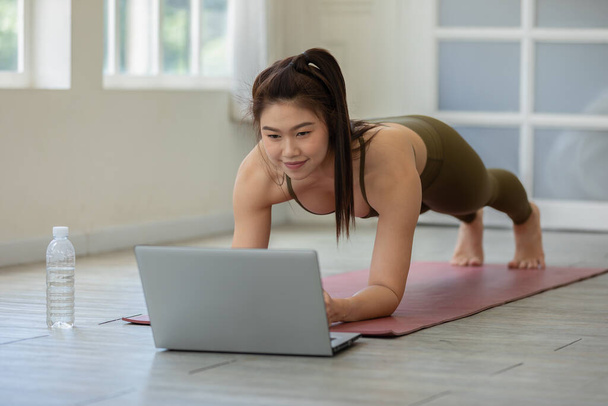 Attractive Asian woman looking laptop practice yoga plank online course at home to meditation comfortable and relax - Фото, изображение