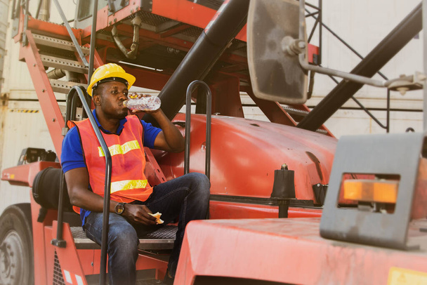 Работники-афроамериканцы носят безопасную одежду на складе, перевозя грузовые контейнеры, экспертизу, опыт вождения в течение дня. - Фото, изображение