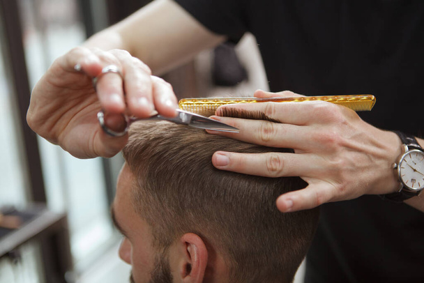 Nahaufnahme eines Friseurs, der einem männlichen Kunden mit der Schere die Haare schneidet - Foto, Bild