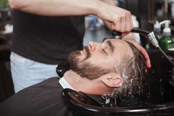 Homme barbu profitant d'un lavage de cheveux par un coiffeur professionnel au salon - Photo, image