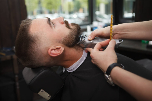 Cliente masculino relaxante enquanto barbeiro profissional aparar sua barba
 - Foto, Imagem
