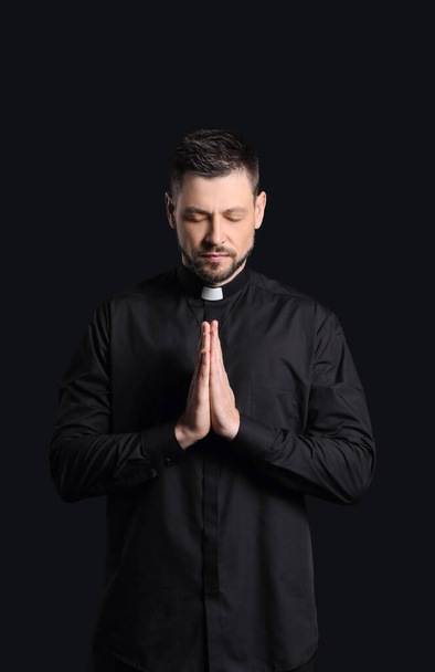 Handsome praying priest on dark background - 写真・画像