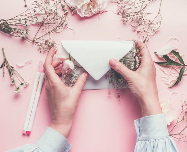 Women hands holding paper envelope filled with  flowers , top view, flat lay.Wedding, invitation ,Valentine day,  Mother's Day  concept. Flat lay, top view, copy space - 写真・画像