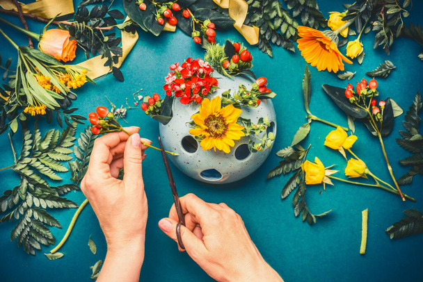 Női kéz, hogy őszi virágok elrendezése kék virágüzlet munkaterület háttér, felülnézet - Fotó, kép