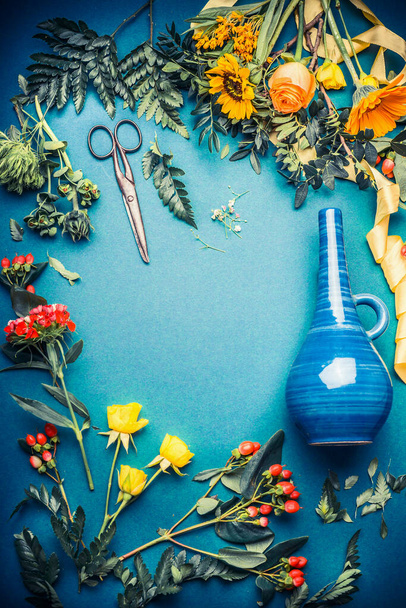 Florist workspace with a lot of autumn flowers and leaves, scissors and  vase on blue background, top view, frame - 写真・画像