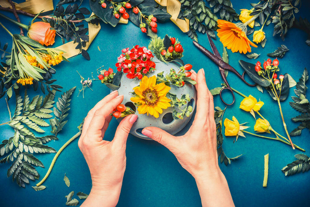Female hand making autumn flowers  arrangements at blue florist workspace background, top view - 写真・画像