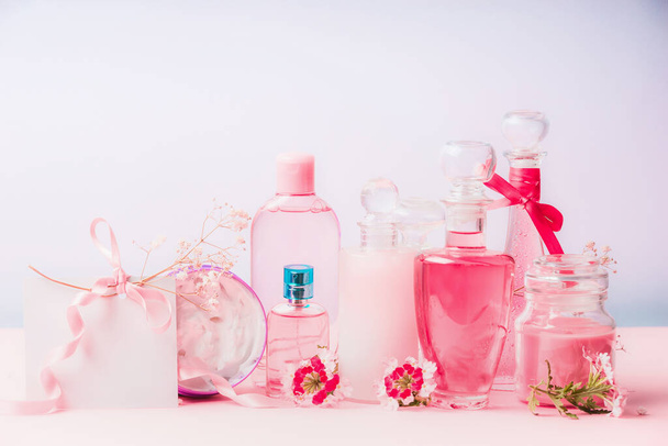 Various natural cosmetic products in bottles and jars with pink flowers at pastel background, front view. Beauty and skin care concept on pastel background, front view - Foto, afbeelding