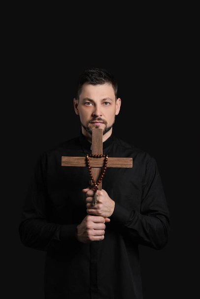 Handsome priest with cross on dark background - Photo, Image