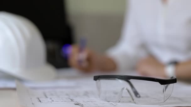 Ο κατασκευαστής σημειώνει στα σχέδια, κάθεται στο γραφείο με τα γυαλιά ασφαλείας σε πρώτο πλάνο - Πλάνα, βίντεο